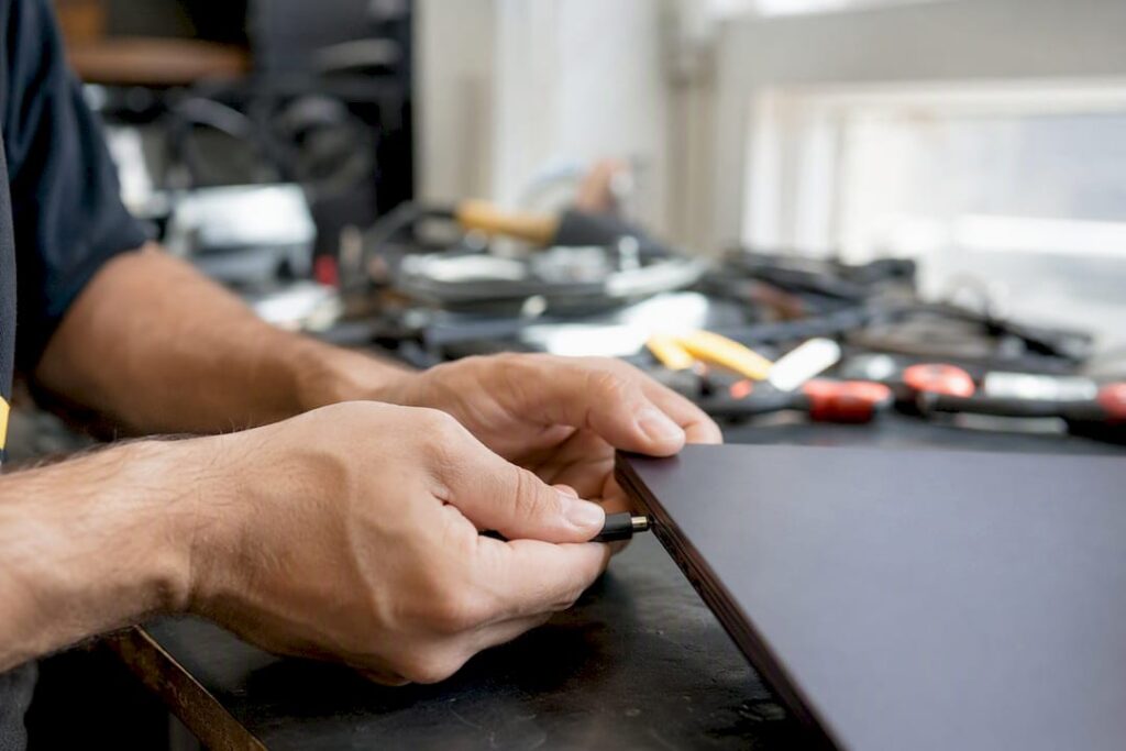 Manos comprobando la conexión del cable de carga de una laptop